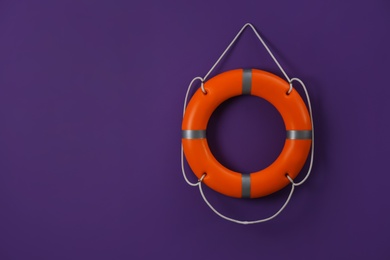 Photo of Orange lifebuoy and space for text on violet background. Rescue equipment