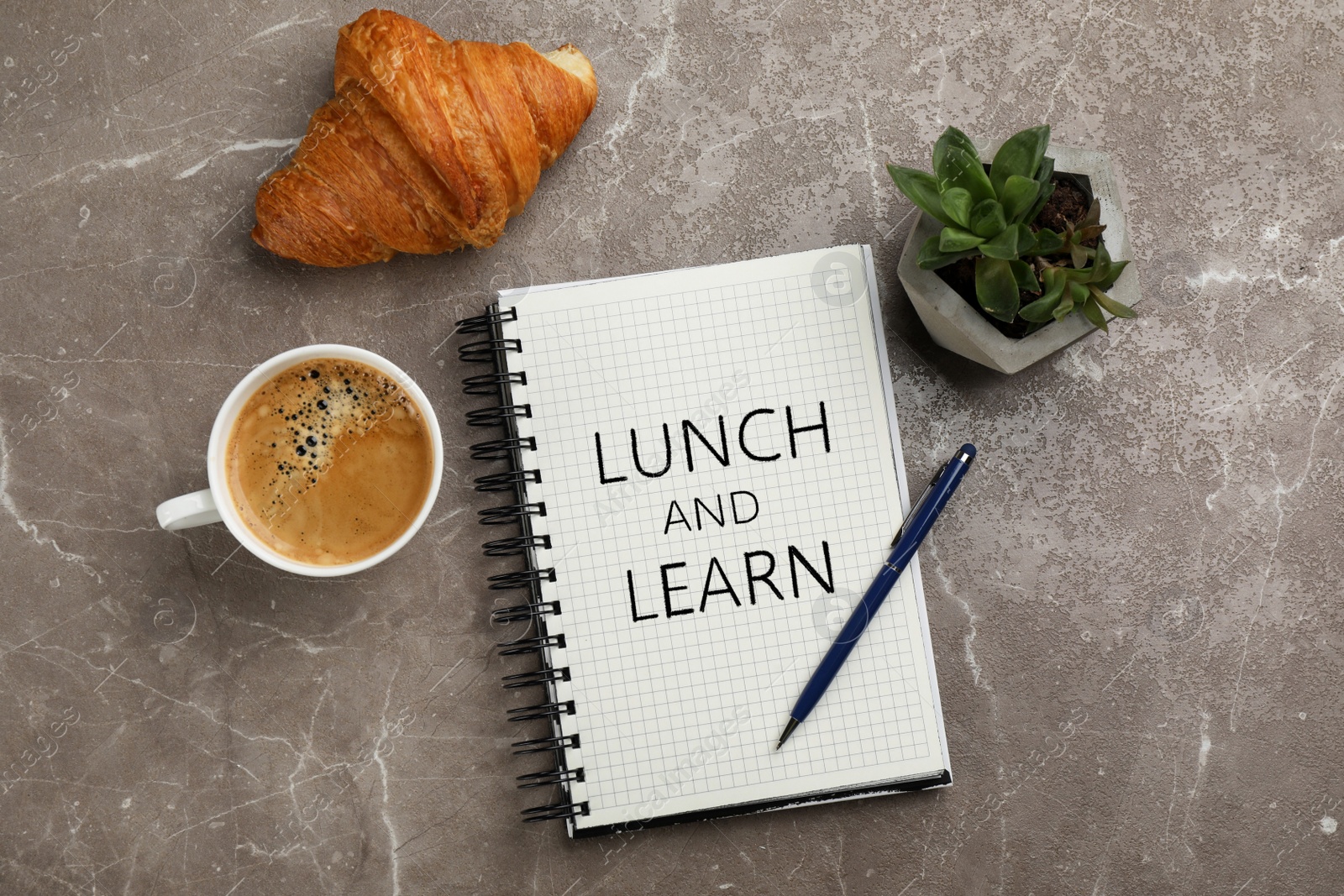 Image of Lunch and Learn concept. Notebook, cup of aromatic coffee, delicious croissant and plant on brown marble table, flat lay