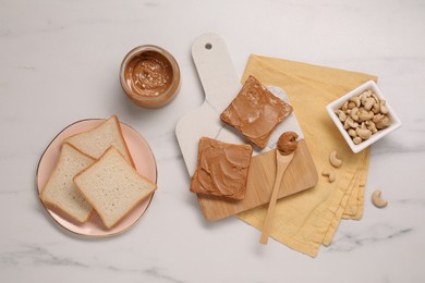Photo of Toasts with tasty nut butter and cashews on white marble table, flat lay