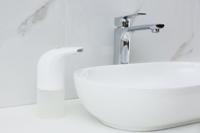 Modern automatic soap dispenser near sink in bathroom, closeup