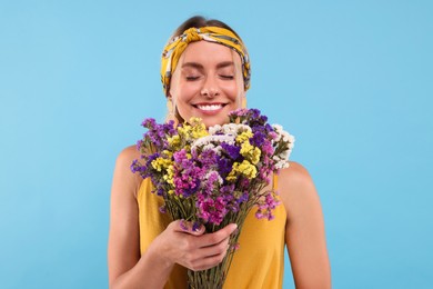Photo of Portrait of smiling hippie woman with bouquet of flowers on light blue background