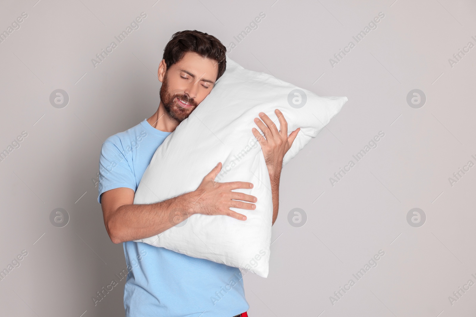 Photo of Sleepy handsome man hugging soft pillow on light grey background