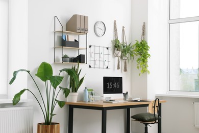 Cozy workplace with computer, modern furniture and houseplants at home