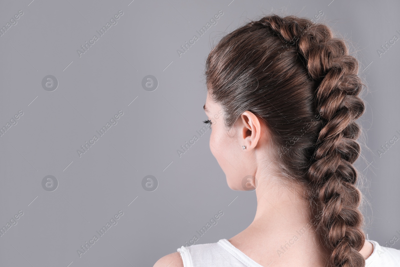 Photo of Woman with braided hair on grey background, back view. Space for text