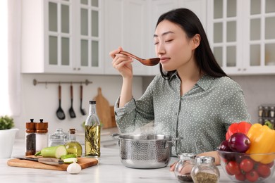 Beautiful woman tasting food after cooking in kitchen