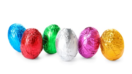 Photo of Many chocolate eggs wrapped in bright foil on white background