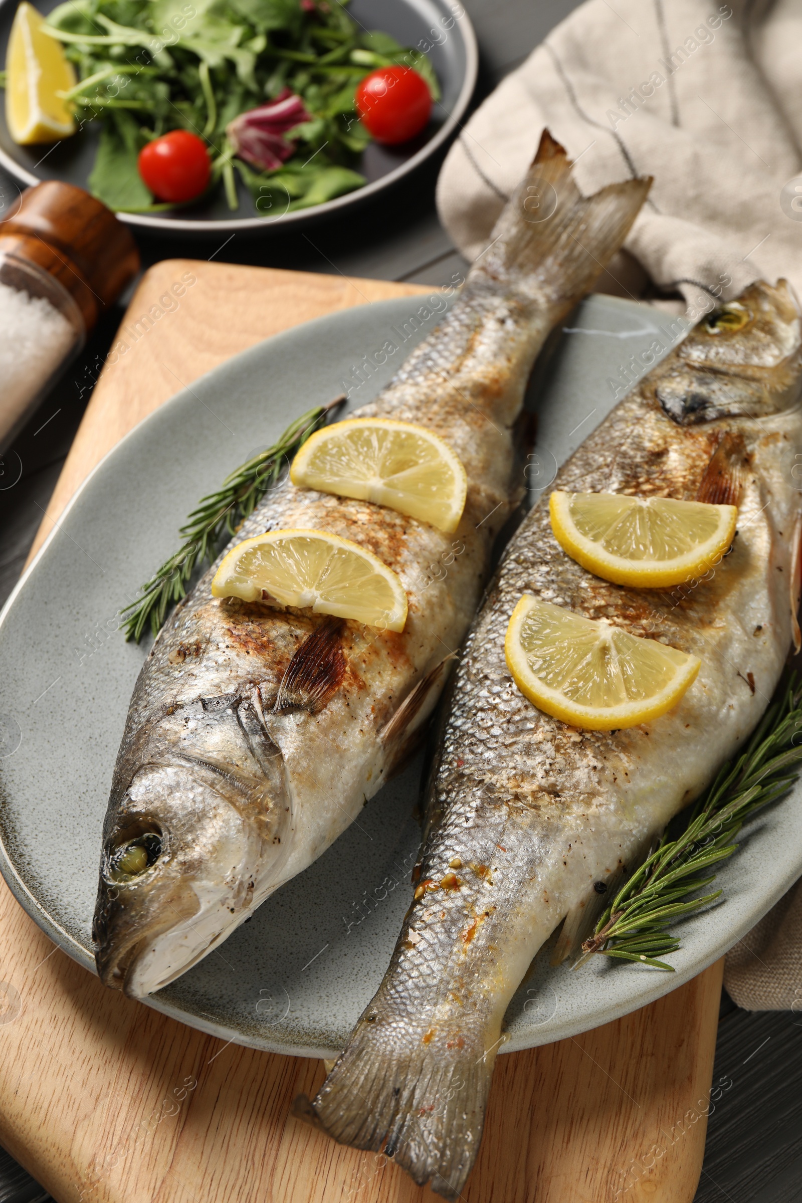 Photo of Delicious baked fish, lemon and rosemary on table