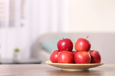 Photo of Plate with sweet red apples on table in room, space for text