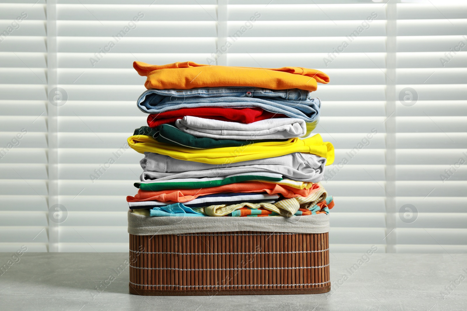 Photo of Laundry basket with clean clothes on light grey table indoors