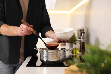 Photo of Man pouring delicious tomato soup into bowl in kitchen, closeup