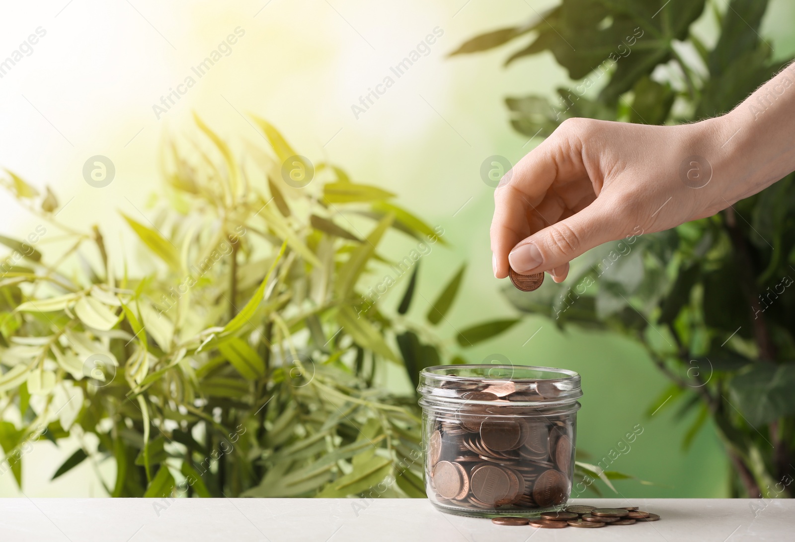 Photo of Woman putting coin into jar on table against blurred background, closeup. Space for text