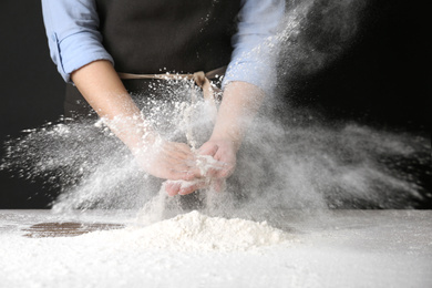 Photo of Woman working with flour at table against black background, closeup