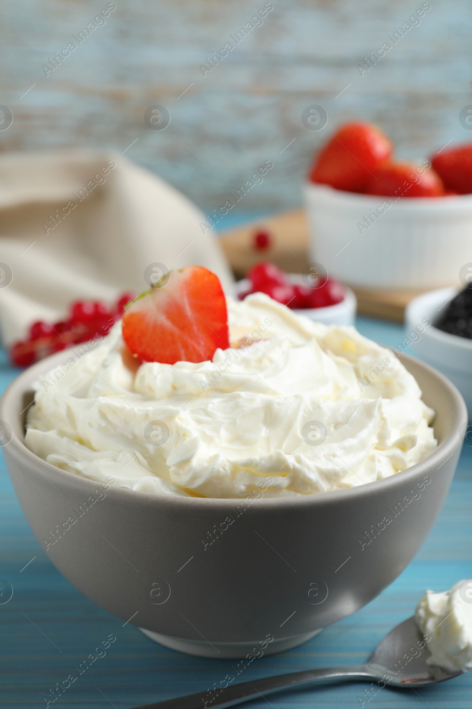 Photo of Tasty cream cheese and fresh berries on light blue wooden table