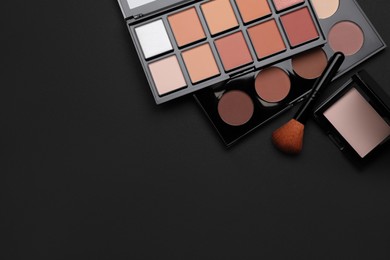 Photo of Different contouring palettes and brush on black background, flat lay with space for text. Professional cosmetic product