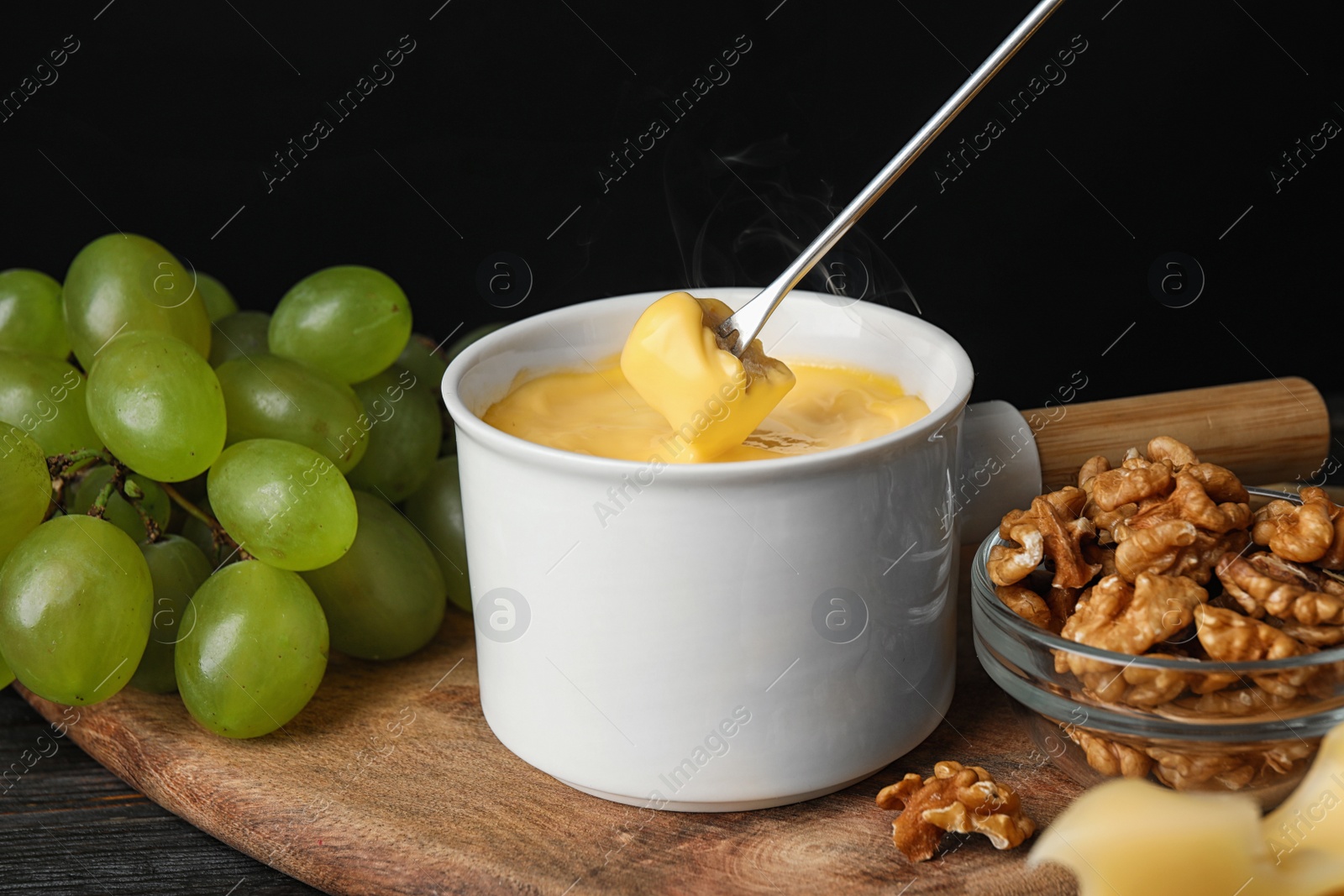 Photo of Pot of tasty cheese fondue and fork with bread on black wooden table