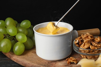 Pot of tasty cheese fondue and fork with bread on black wooden table