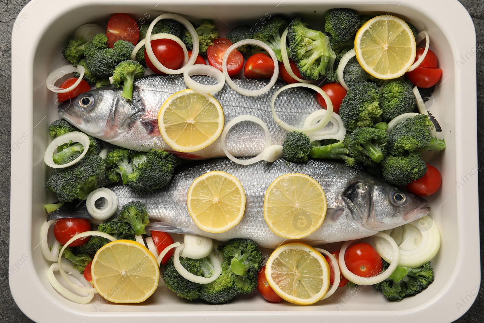 Photo of Raw fish with vegetables and lemon in baking dish on table, top view