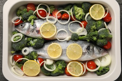 Raw fish with vegetables and lemon in baking dish on table, top view