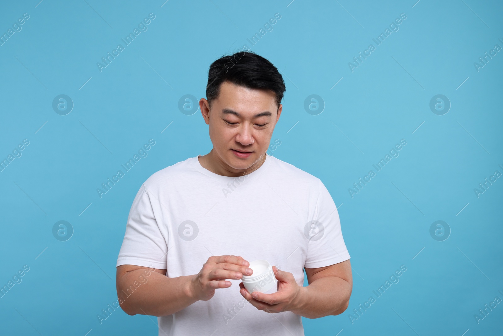 Photo of Handsome man with jar of body cream on light blue background