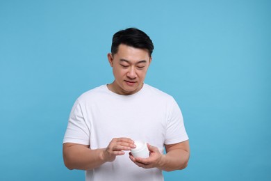 Photo of Handsome man with jar of body cream on light blue background