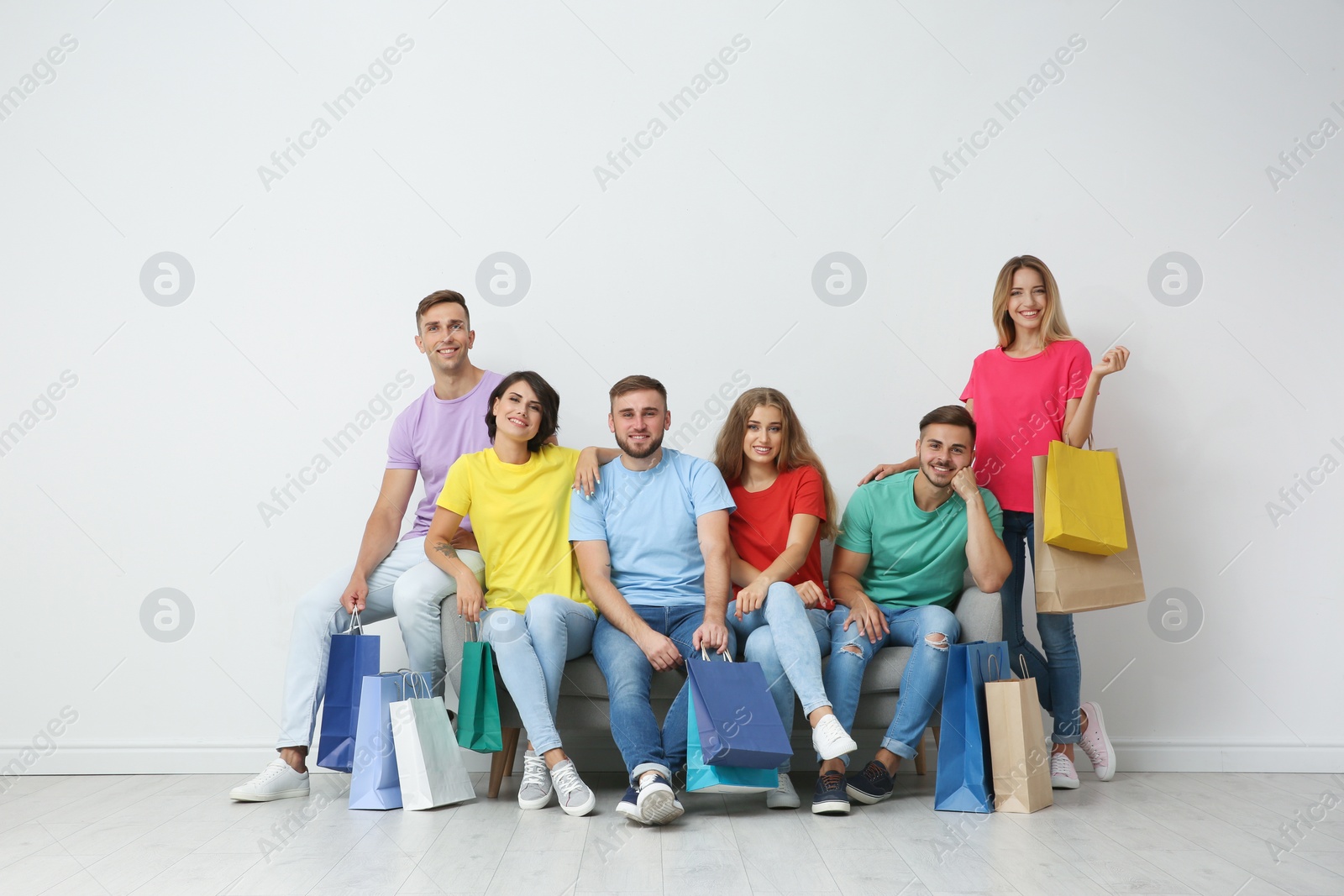 Photo of Group of young people with shopping bags sitting on sofa near light wall