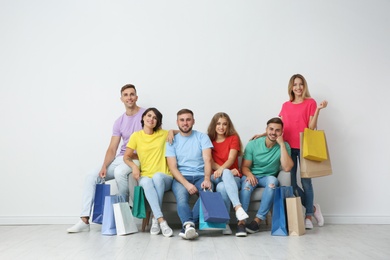 Group of young people with shopping bags sitting on sofa near light wall