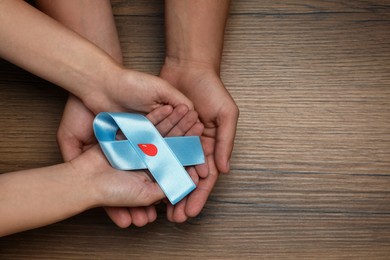 Photo of People holding light blue ribbon with paper blood drop at wooden table, top view and space for text. Diabetes awareness
