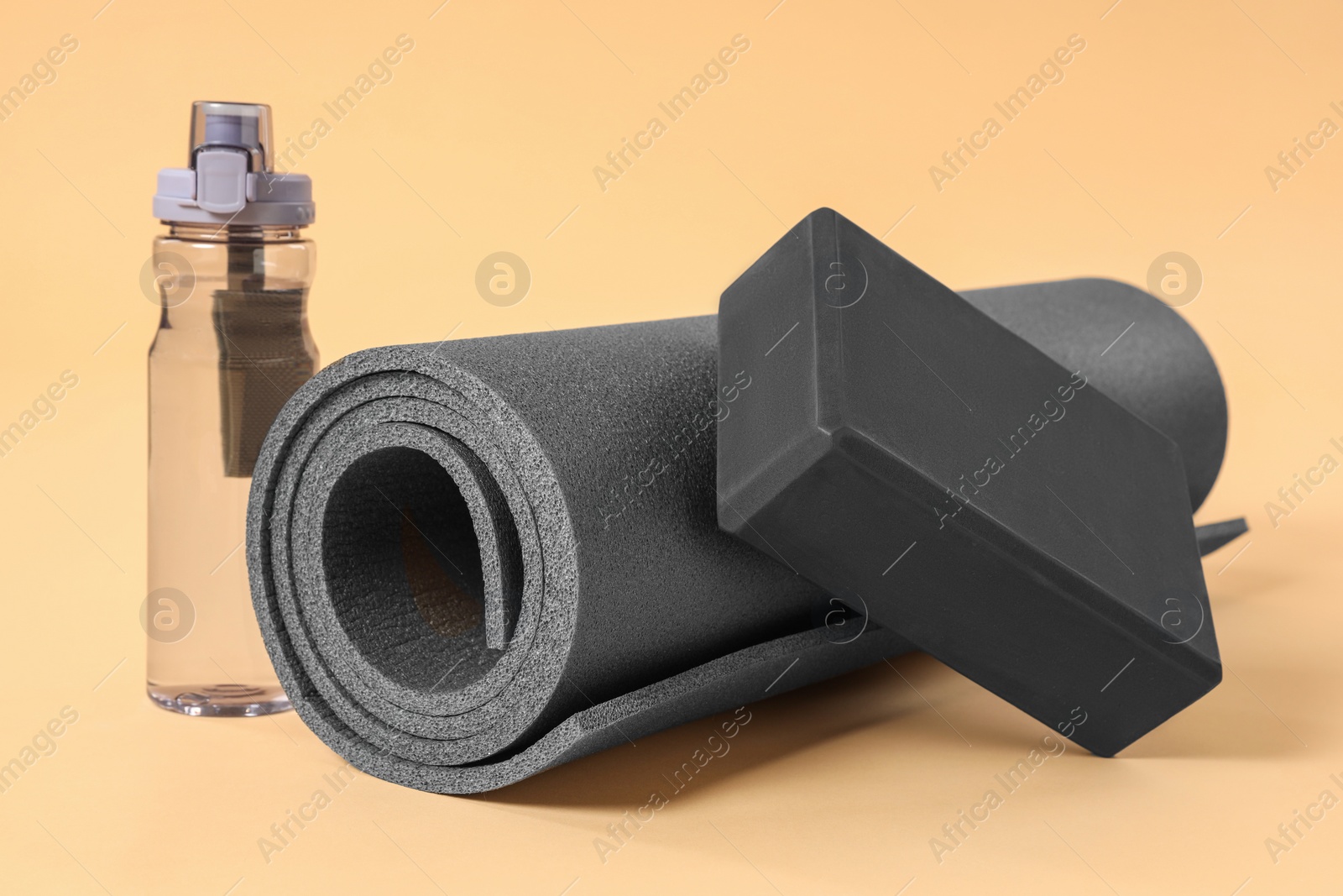 Photo of Grey exercise mat, yoga block and bottle of water on beige background