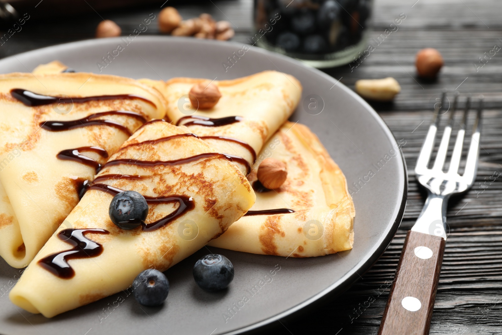 Photo of Delicious thin pancakes with chocolate, blueberries and nuts on black wooden table, closeup