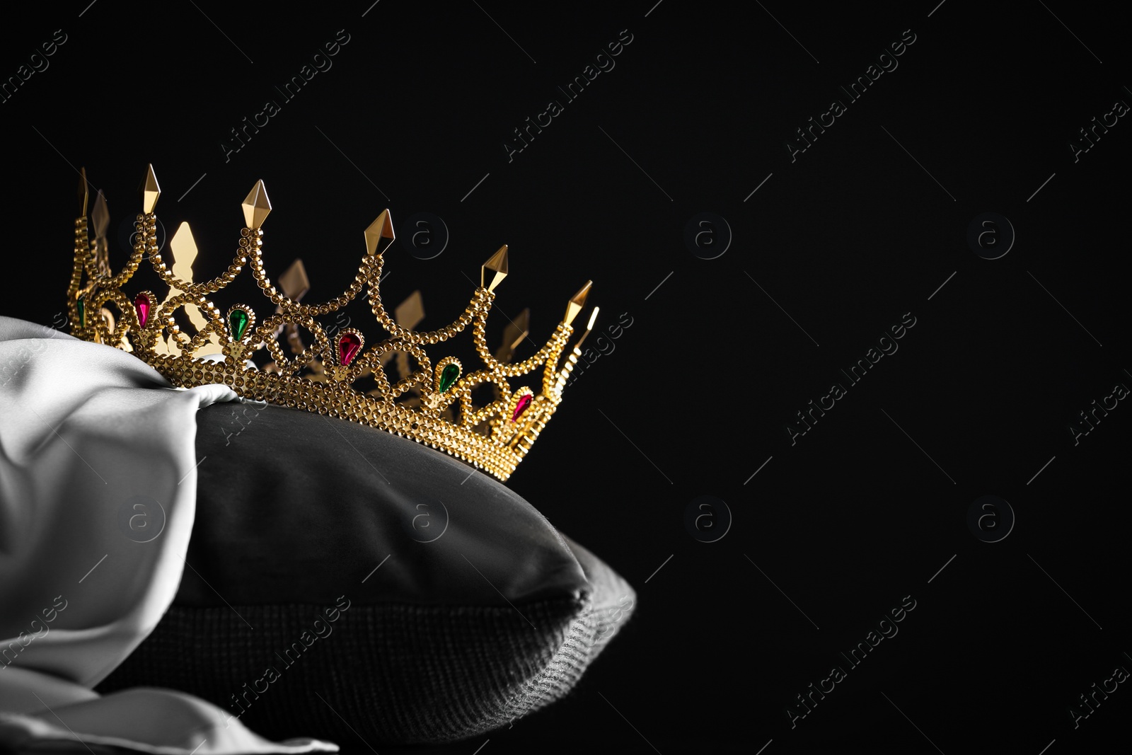 Photo of Beautiful gold crown with gems on pillow against black background. Space for text