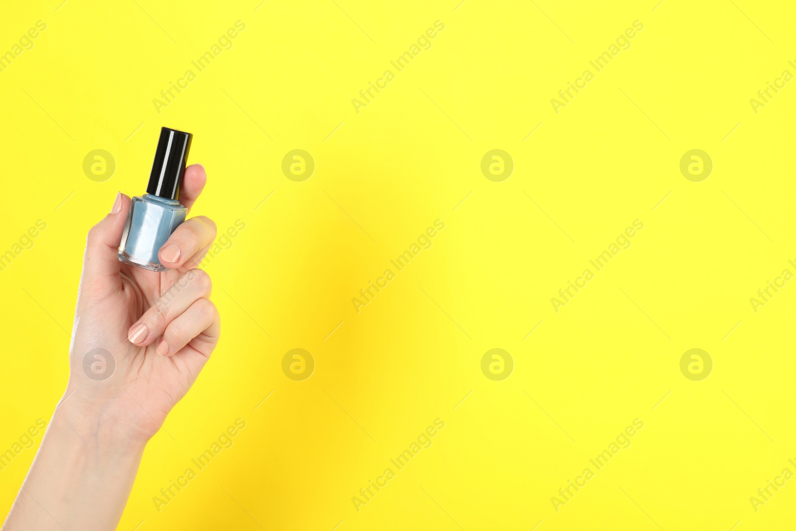 Photo of Woman holding nail polish on yellow background, closeup. Space for text