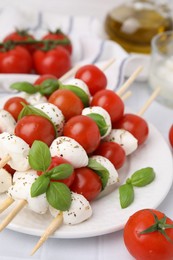 Photo of Caprese skewers with tomatoes, mozzarella balls, basil and spices on white table, closeup