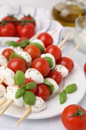 Caprese skewers with tomatoes, mozzarella balls, basil and spices on white table, closeup