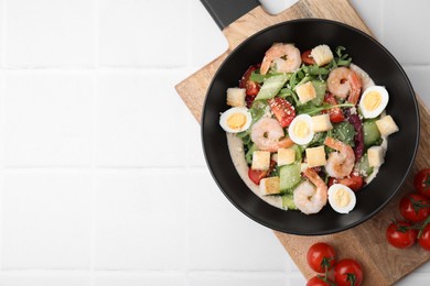 Delicious Caesar salad with shrimps and tomatoes on white tiled table, top view. Space for text