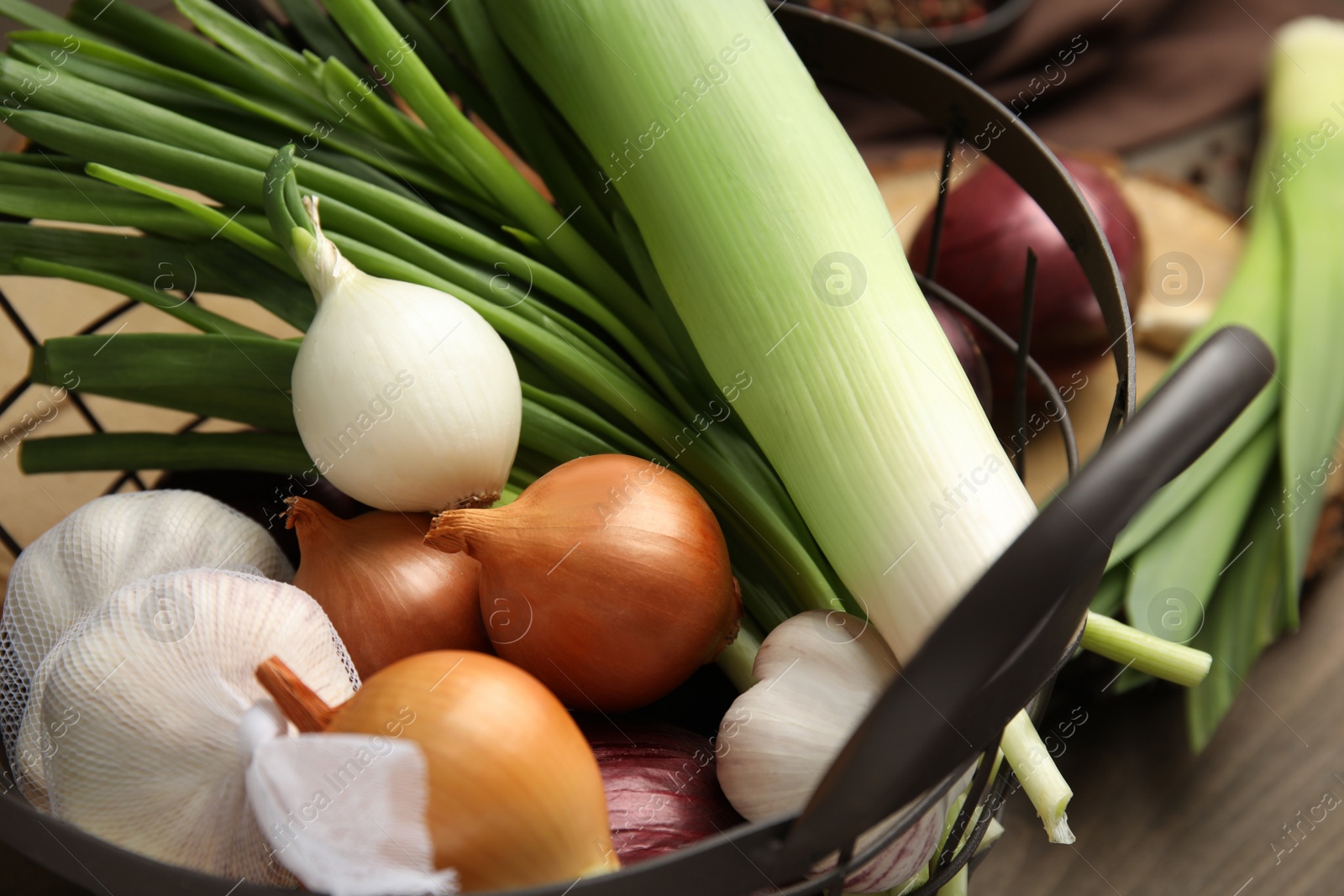 Photo of Metal basket with fresh onion bulbs, leek and garlic on wooden table, closeup