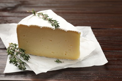 Photo of Piece of tasty camembert cheese and thyme on wooden table, closeup