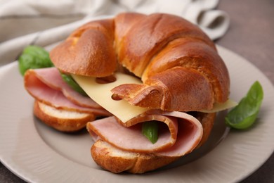 Photo of Tasty crescent roll with ham, cheese and basil on plate, closeup