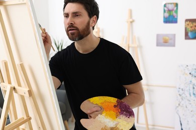 Photo of Man painting in studio. Using easel to hold canvas