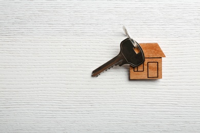 Photo of Key with trinket in shape of house on wooden background. Real estate agent services