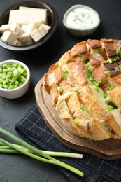 Photo of Freshly baked bread with tofu cheese and green onions on black table, closeup