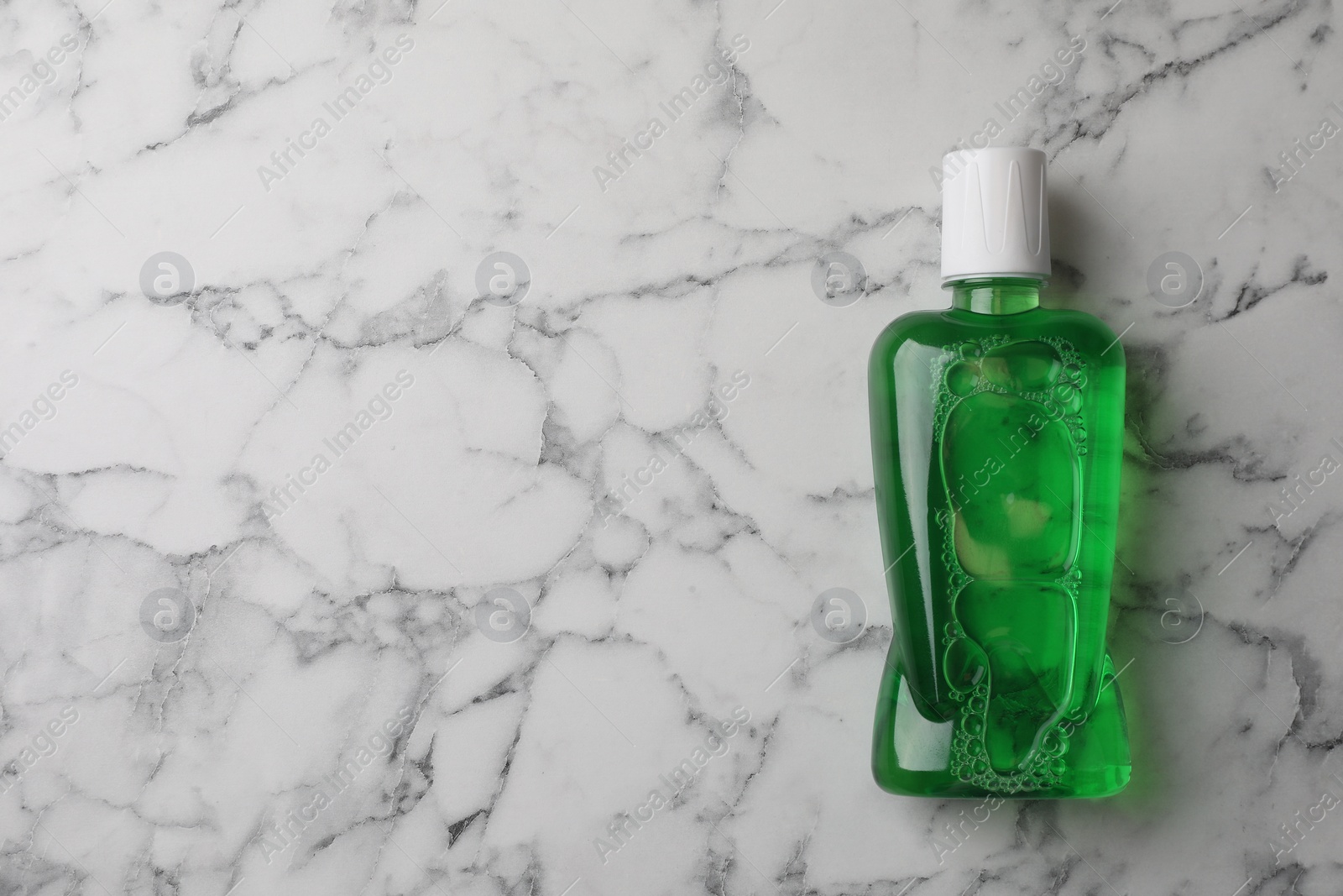Photo of Fresh mouthwash in bottle on white marble table, top view. Space for text