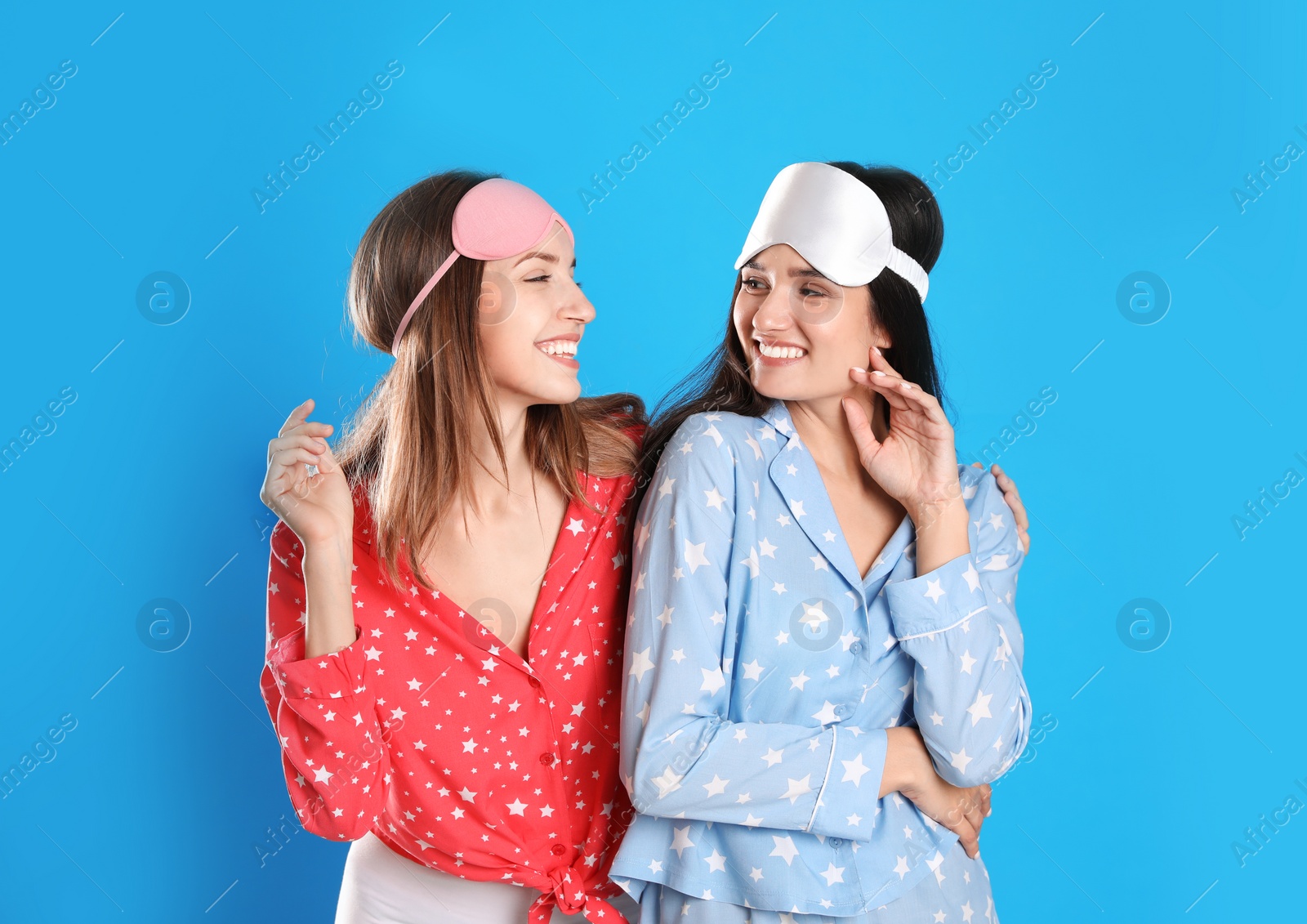Photo of Beautiful women wearing sleeping masks on light blue background. Bedtime