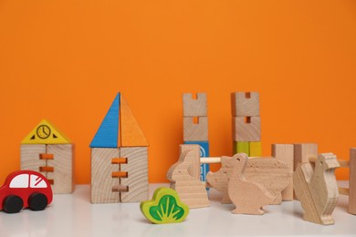 Photo of Set of wooden toys on white table near orange wall, closeup. Children's development