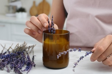 Photo of Woman decorating homemade candle with lavender flowers at table indoors, closeup