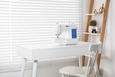 Photo of Sewing machine on white desk near chair indoors