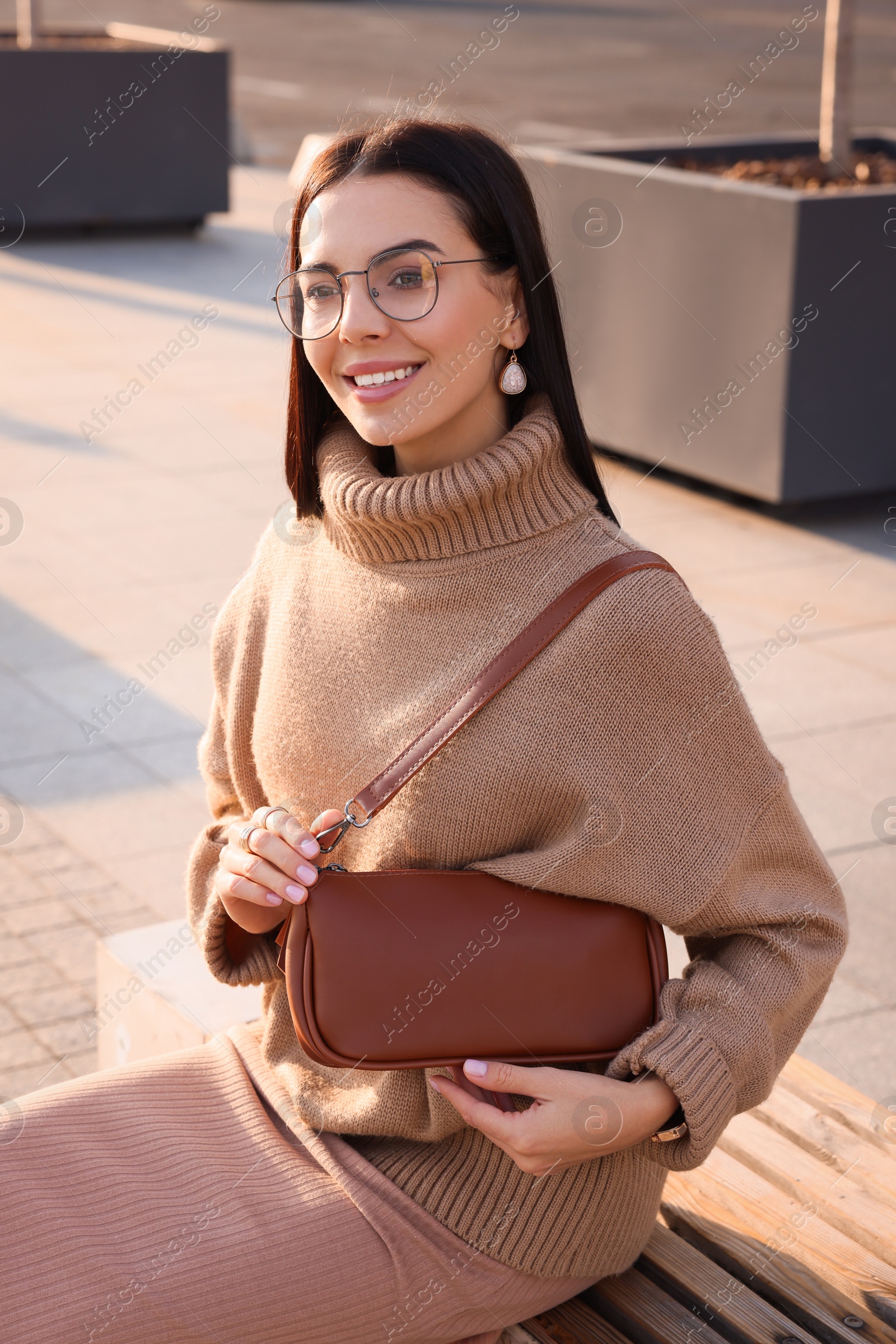 Photo of Fashionable young woman with stylish bag on bench outdoors