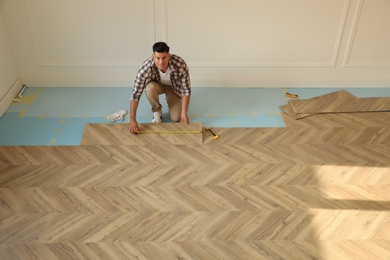 Photo of Professional worker installing new parquet flooring indoors, above view