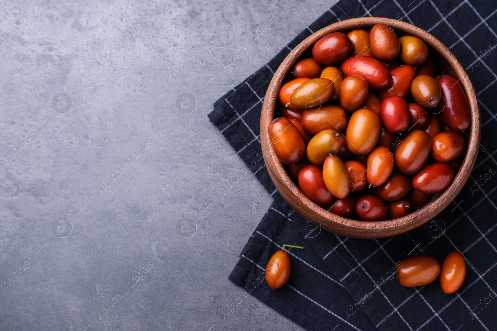 Photo of Wooden bowl of ripe red dates and napkin on grey table, top view. Space for text