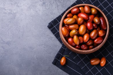 Wooden bowl of ripe red dates and napkin on grey table, top view. Space for text