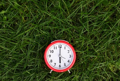 Red alarm clock on green grass outdoors, top view. Space for text